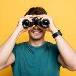 Person holding binoculars to their eyes with a smile